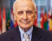 Headshot of white older male with dark suite and yellow and blue patterned tie.