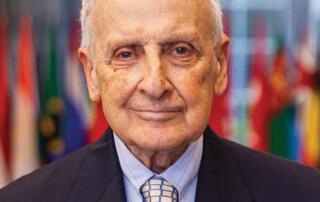 Headshot of white older male with dark suite and yellow and blue patterned tie.